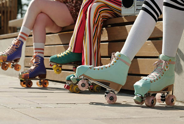 Legs of three girls in roller skates and casualwear sitting on bench in park on sunny summer day and having break after training or stroll